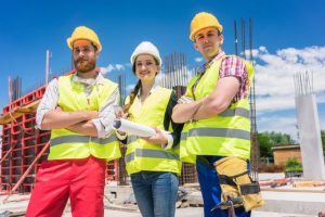 Portrait of three confident and reliable young employees, a female architect and two blue-collar workers, looking at camera while posing on the construction site