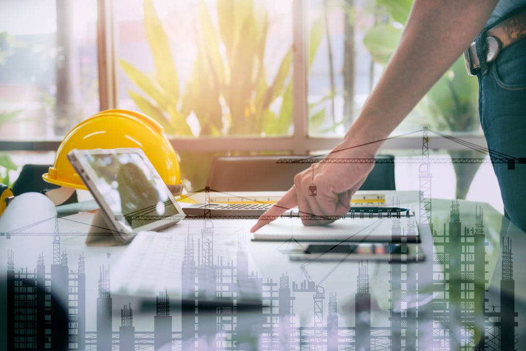 notepad and tablet on desk with hard hat and construction graphics overlay