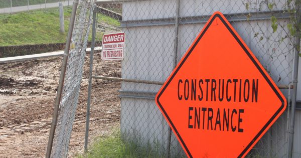 Construction entrance warning sign against a metal fence